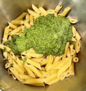 pesto sauce being mixed with hot fresh pasta